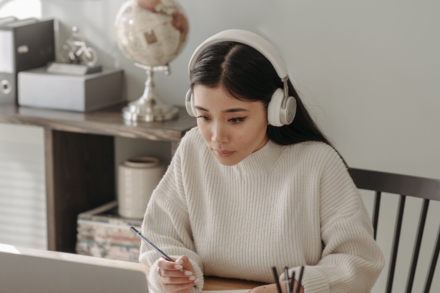 Una mujer con auriculares estudia en casa con un ordenador portátil.